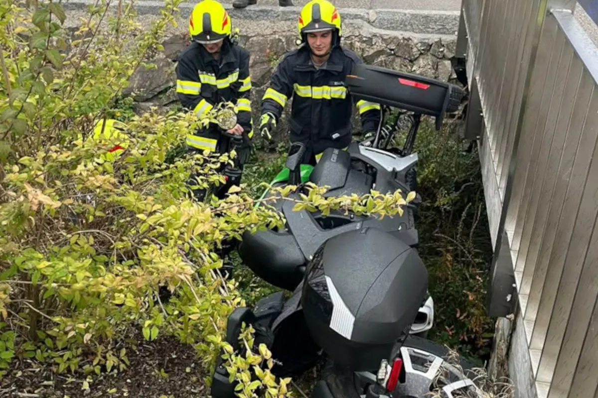 Zwei Feuerwehrleute in Einsatzkleidung bergen einen Roller, der in dichtem Gebüsch neben einer Mauer liegt.