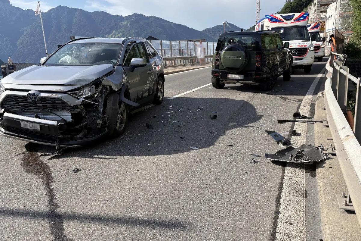 Ein silbernes Auto mit Frontschaden steht auf einer Bergstraße; im Hintergrund sind weitere Fahrzeuge sichtbar, darunter ein Rettungswagen.