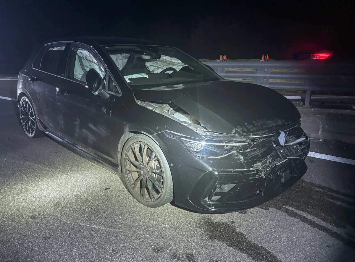 Ein schwarzes Auto mit stark beschädigtem Vorderteil steht bei Nacht auf einer Straße. Die Scheinwerfer sind teilweise zerbrochen und der Airbag ist ausgelöst.