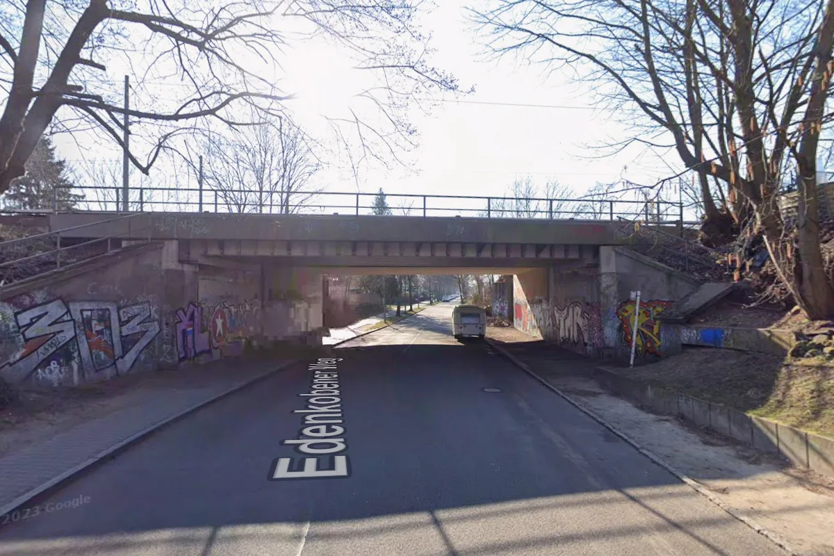 Eine Unterführung mit Graffitis an den Seitenwänden und einem geparkten Wohnwagen auf der Straße. Bäume umrahmen die Szene.