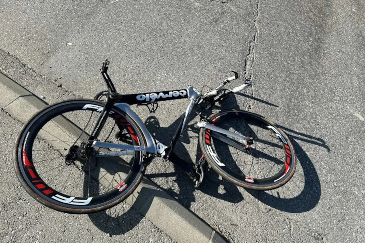 Ein silbernes und schwarzes Rennrad liegt beschädigt auf einer asphaltierten Straße. Es ist stark deformiert.
