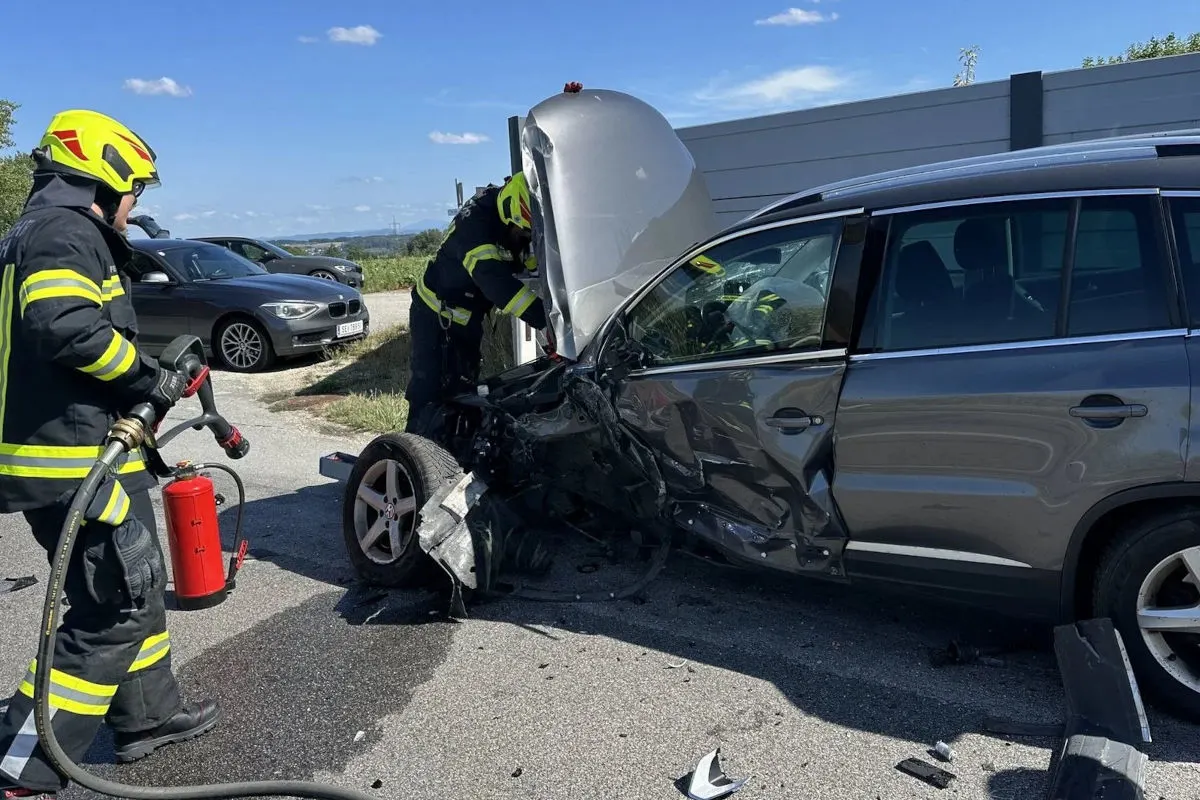 Zwei Feuerwehrleute in Schutzkleidung sind an einem stark beschädigten grauen Auto beteiligt. Der Frontbereich des Wagens zeigt erhebliche Schäden.