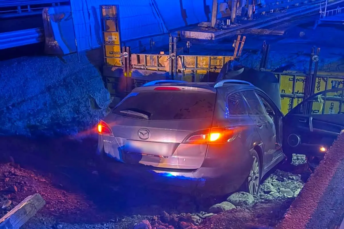 Ein silberner Mazda ist in einer Baugrube neben einer Baustelle festgefahren. Es ist Nacht und das Fahrzeug ist umgeben von blauen Lichtreflexen.