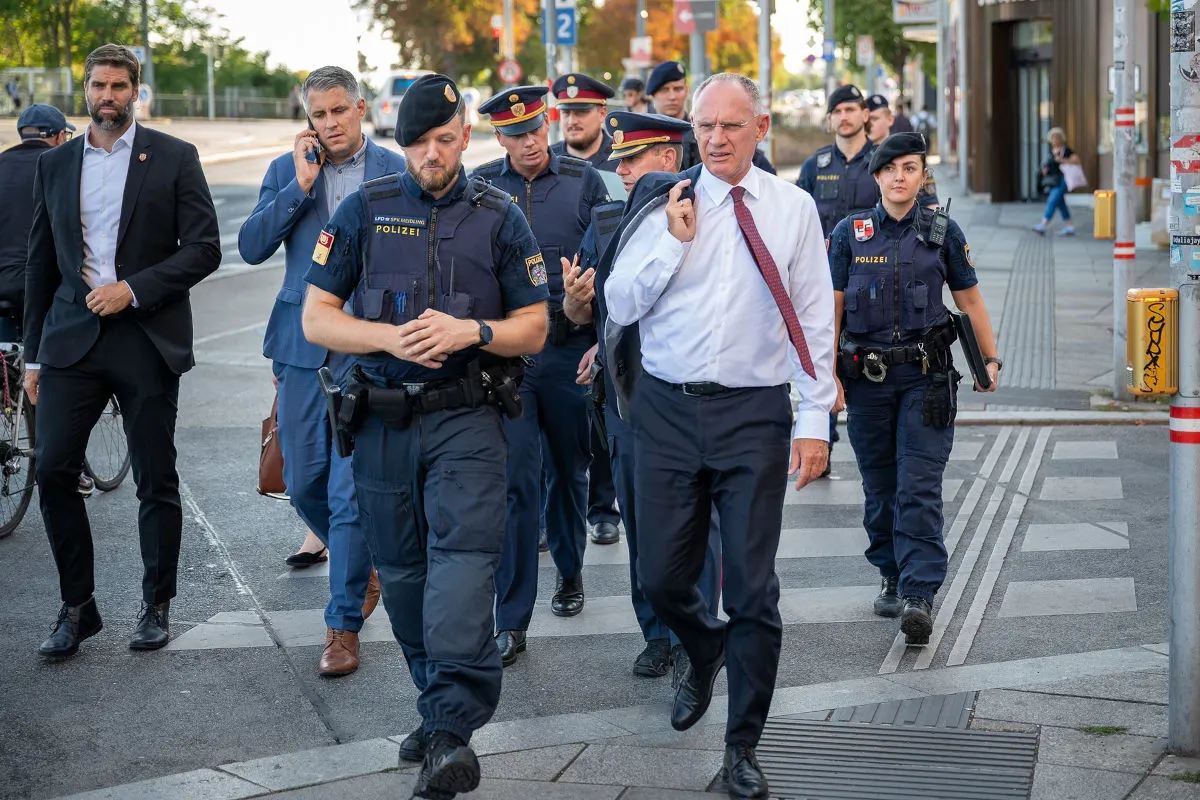 Eine Gruppe von Polizeibeamten in Uniform und mehreren Männern in Anzügen geht einen Gehweg entlang, vermutlich bei einem offiziellen Anlass.