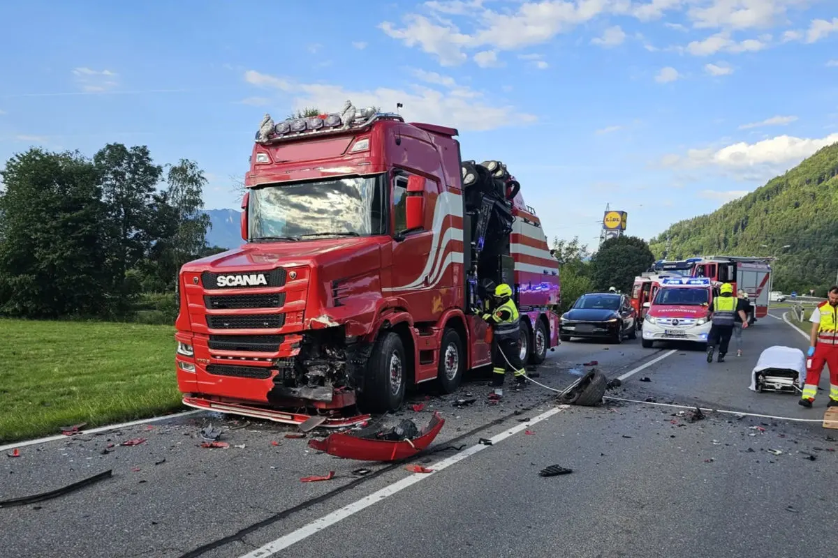Ein roter Scania-LKW steht beschädigt auf einer Straße. Rettungskräfte sind vor Ort, umgeben von Trümmerteilen.