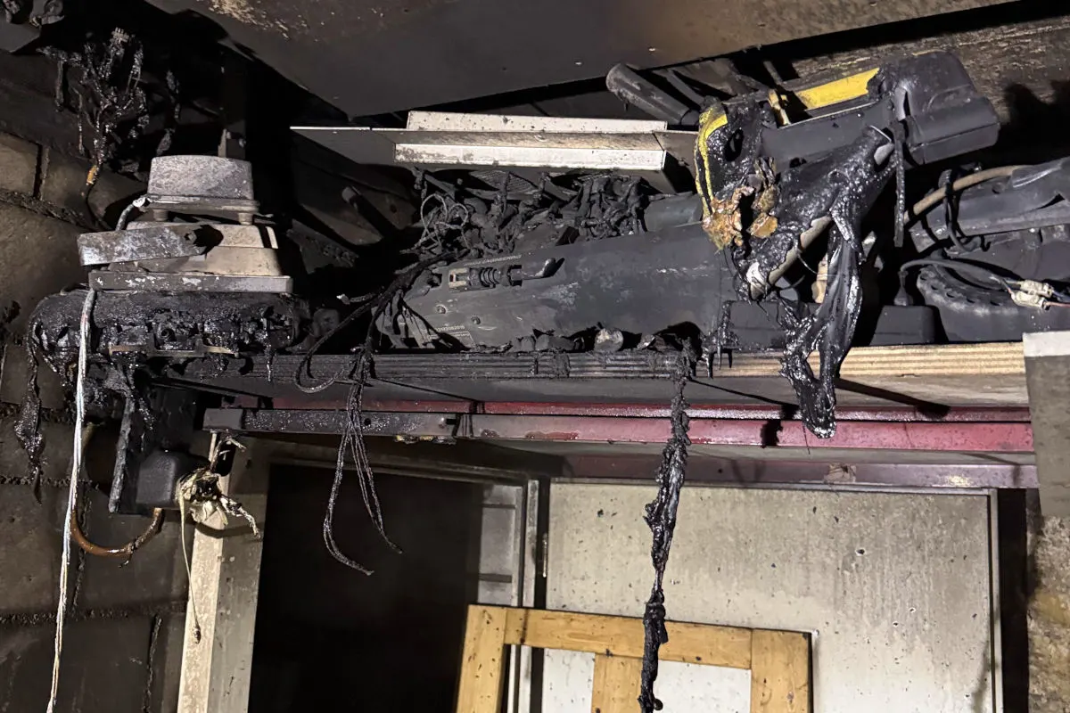 Das Bild zeigt stark verbrannte elektrische Geräte an der Decke eines Raumes. Kabel und Geräte sind geschwärzt und teils geschmolzen.