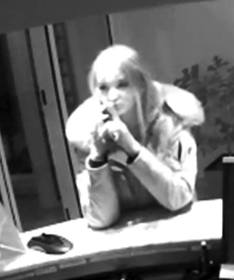 Eine Person mit langen Haaren und einer Winterjacke steht an einem Empfangstresen und schaut in die Kamera.