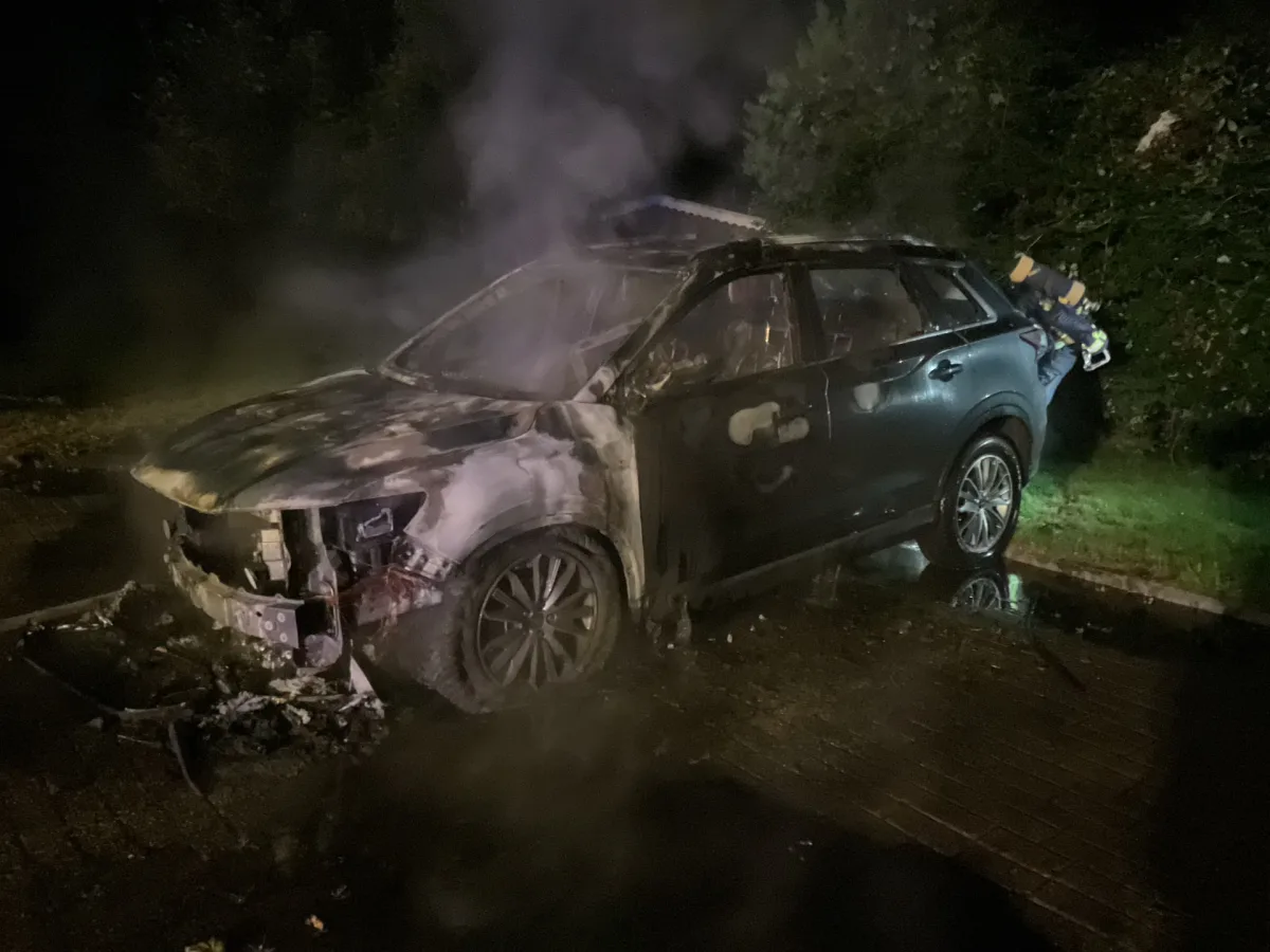 Ein Fahrzeug ist stark ausgebrannt und raucht noch, es steht auf einer Straße bei Nacht.