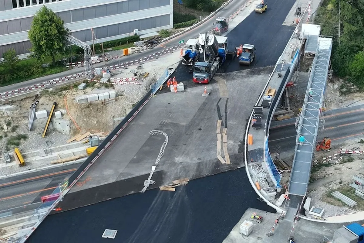 Mehrere Maschinen sind bei Bauarbeiten auf einer frisch asphaltierten Straße zu sehen, umgeben von Baustellenmaterialien.