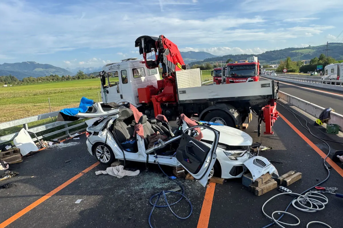 Ein schwer beschädigtes Auto liegt neben einem großen Kranfahrzeug auf einer Autobahn. Trümmer sind verstreut.