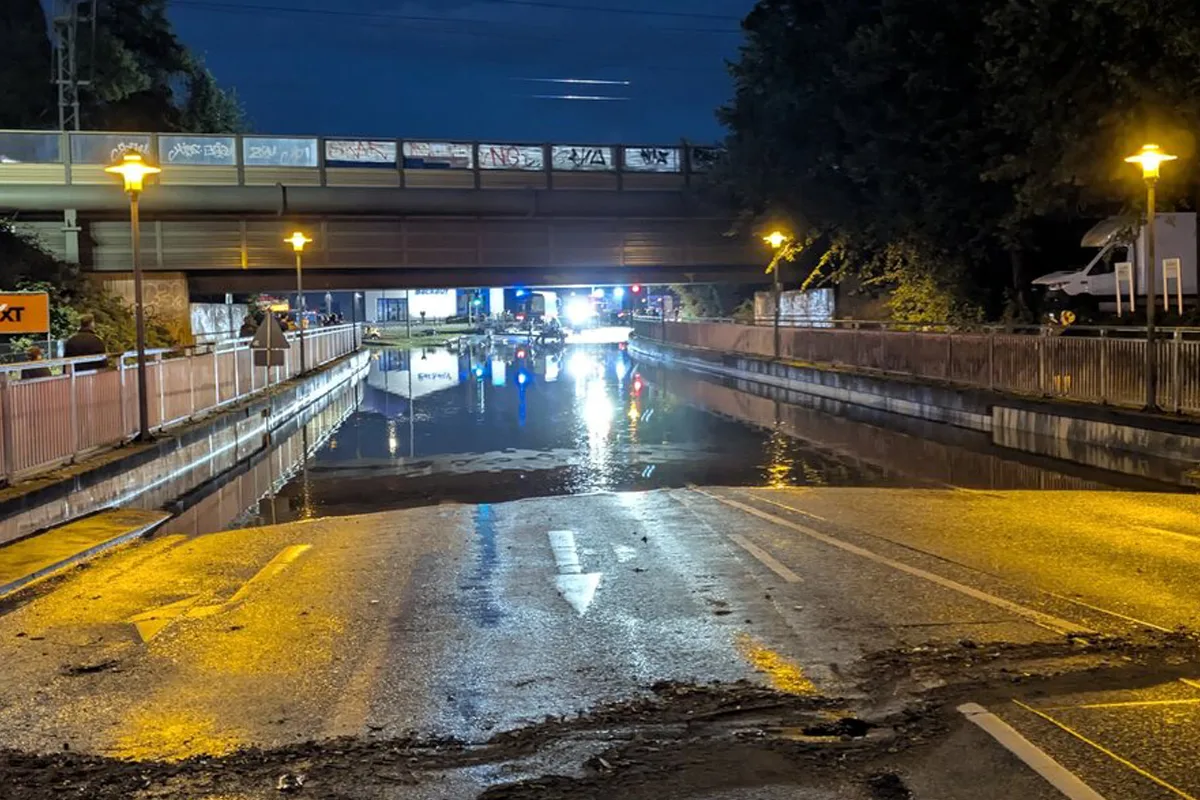 Eine tief stehende Straße unter einer Brücke ist komplett mit Wasser bedeckt, beleuchtet von Straßenlaternen in der Dunkelheit.
