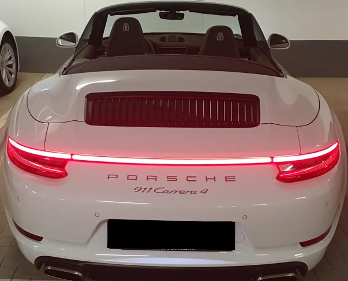 Ein weißer Porsche 911 Carrera 4 ist von hinten in einer Garage zu sehen. Die Rückleuchten sind rot beleuchtet, und das Dach ist geöffnet.