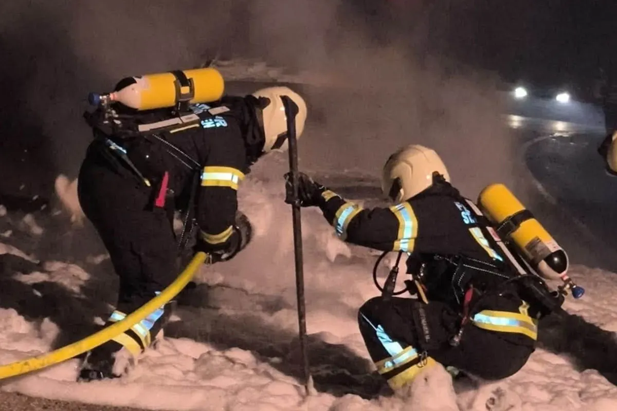 Zwei Feuerwehrleute in Einsatzkleidung bekämpfen nachts mit Schaum einen Brand. Sie tragen Atemschutzgeräte.