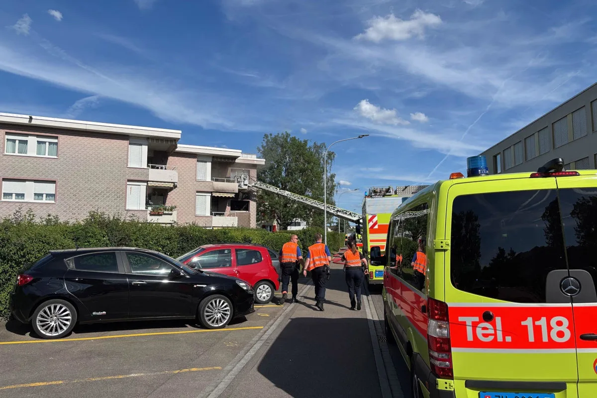 Mehrere Personen in orangefarbenen Westen, ein Feuerwehrfahrzeug und eine Drehleiter vor einem Wohngebäude an einem sonnigen Tag.