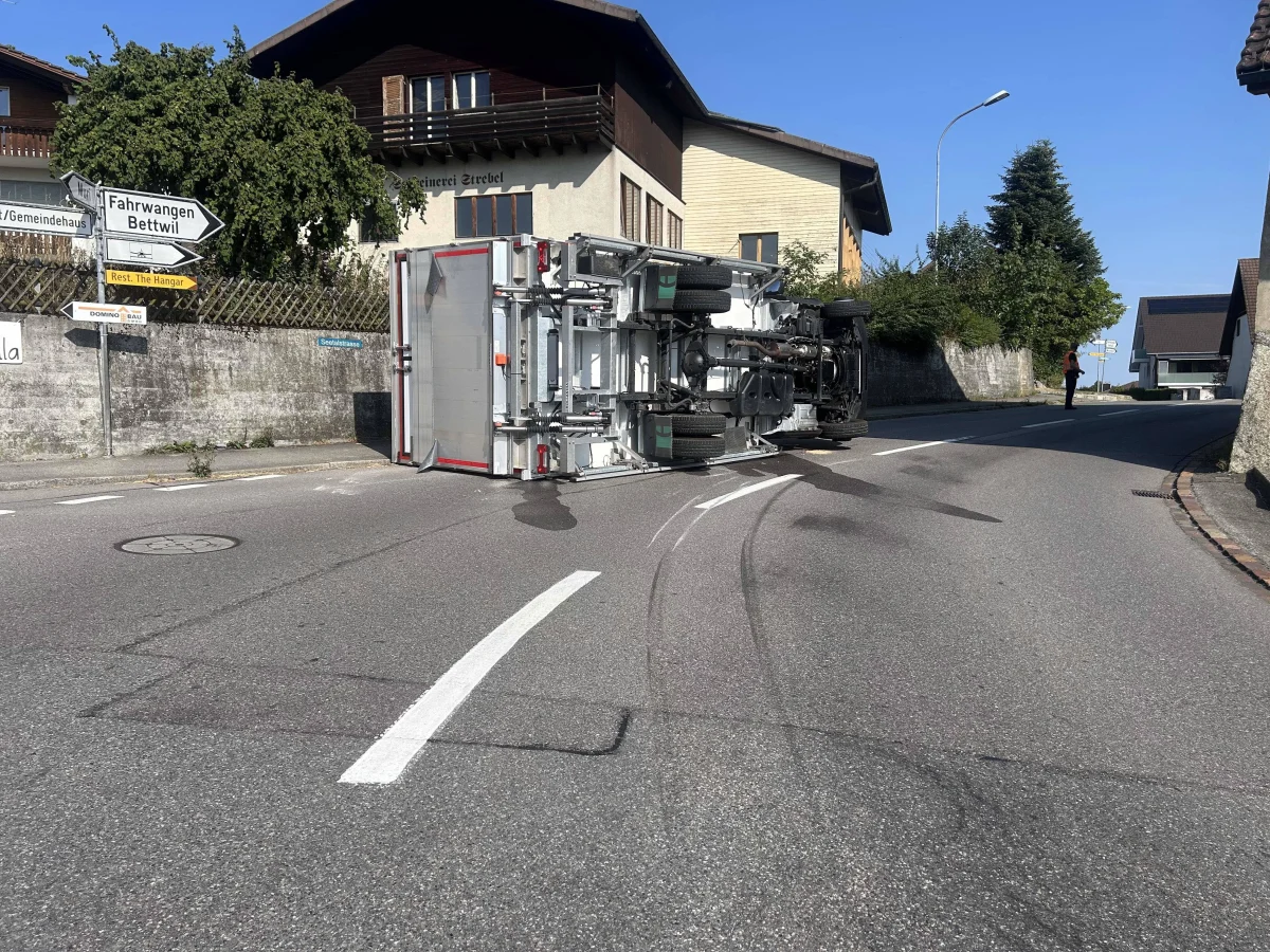 Ein Lastwagen liegt auf der Seite und blockiert die Straße in einer Ortschaft. Ein Verkehrsschild weist auf Fahrwangen und Bettwil hin.