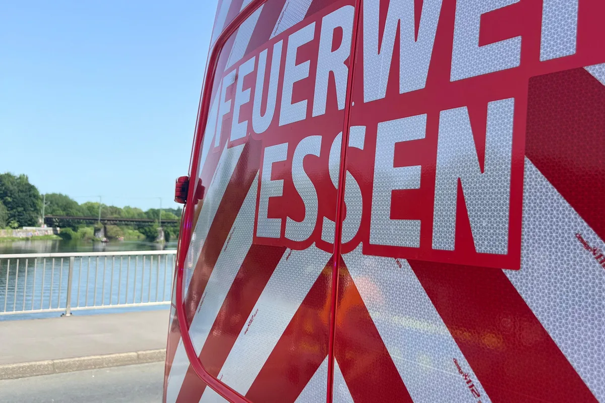 Ein Feuerwehrfahrzeug der Stadt Essen, markiert mit auffälliger rot-weißer Beschriftung, steht am Ufer eines Flusses bei klarem Wetter.