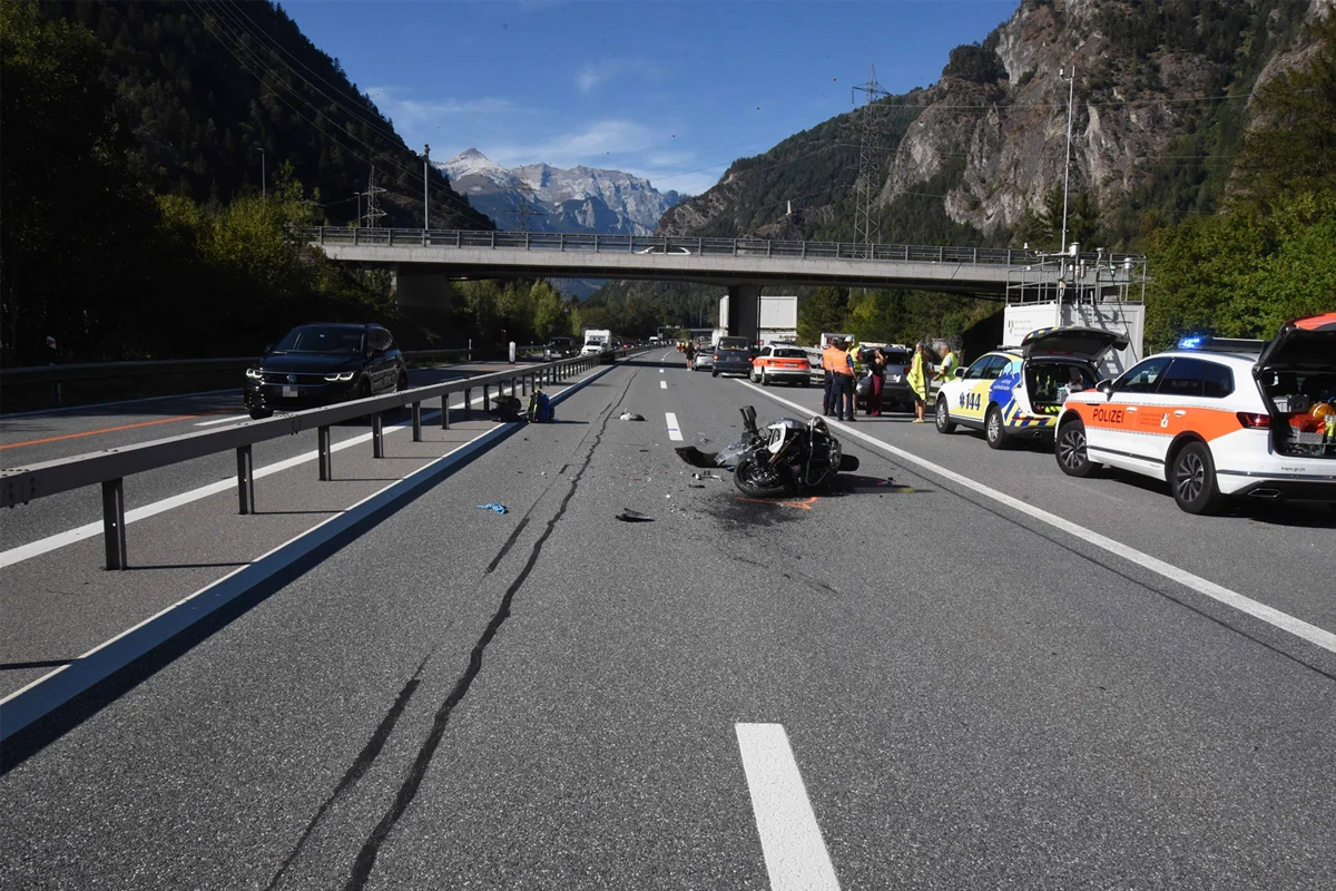 Auf einer Autobahn liegt ein zerstörtes Motorrad, umgeben von Polizeifahrzeugen und Personal. Im Hintergrund sind Berge zu sehen.