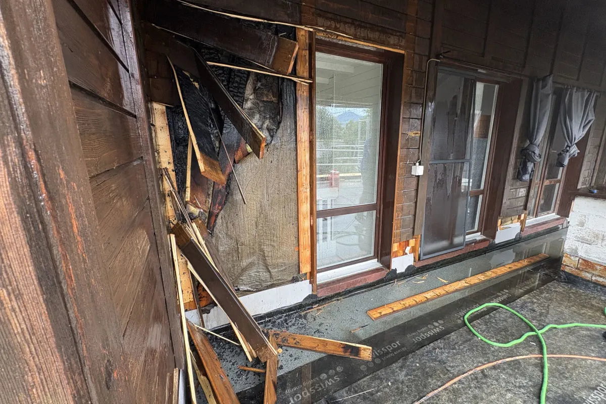 Die Aufnahme zeigt eine Holzwand eines Hauses, die durch ein Feuer stark beschädigt wurde. Die Holzverkleidung ist verkohlt und teilweise eingestürzt.