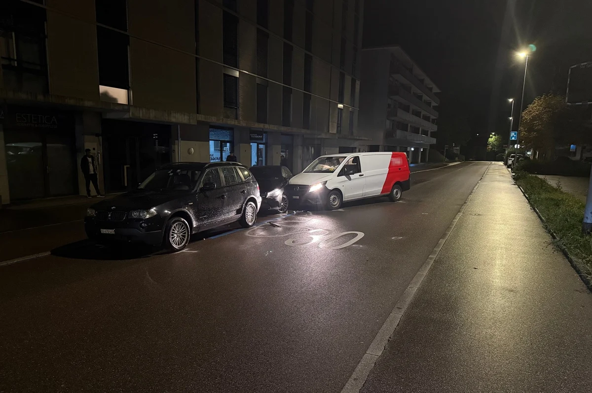 Ein schwarzer PKW und ein weißer Lieferwagen sind auf einer dunklen Straße zusammengestoßen. Beide Fahrzeuge zeigen sichtbare Schäden.