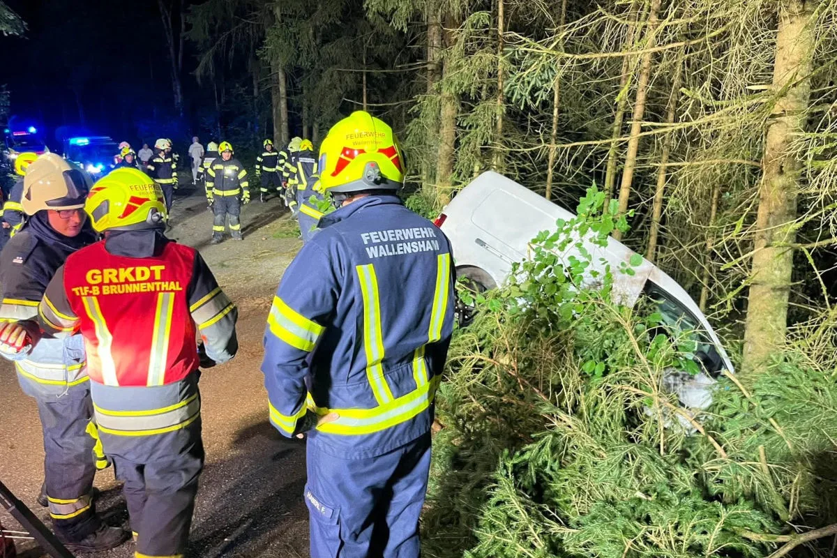 Ein verunfalltes Fahrzeug liegt abseits einer Straße im Wald. Umgeben von mehreren Feuerwehrleuten in Einsatzkleidung bei Nacht.