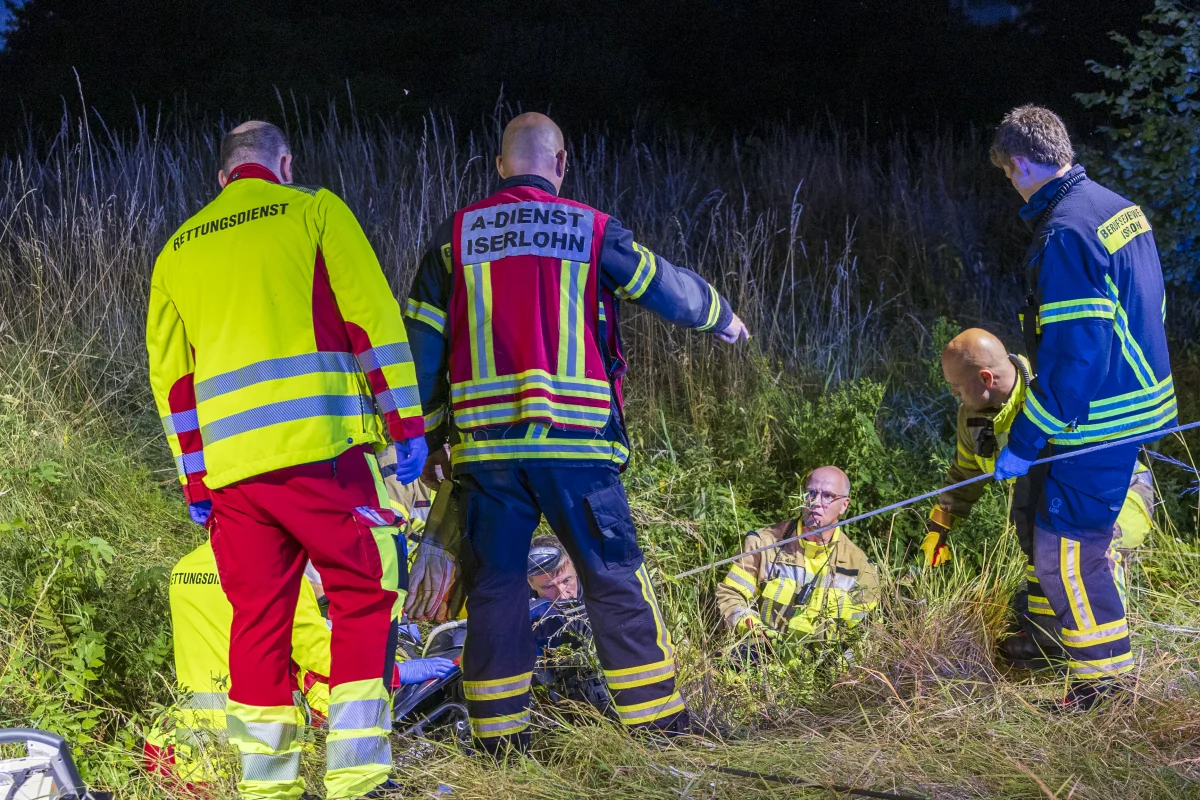 Mehrere Rettungskräfte operieren im hohen Gras, um eine sitzende Person zu bergen. Es ist Nacht und sie tragen Rettungswesten.