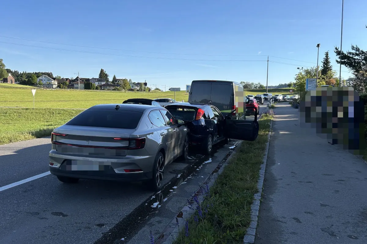 Ein graues Auto, ein blaues Auto und ein Van sind in eine Kollision auf einer Landstraße verwickelt. Die Autos stehen hintereinander auf der Straße bei Tageslicht.