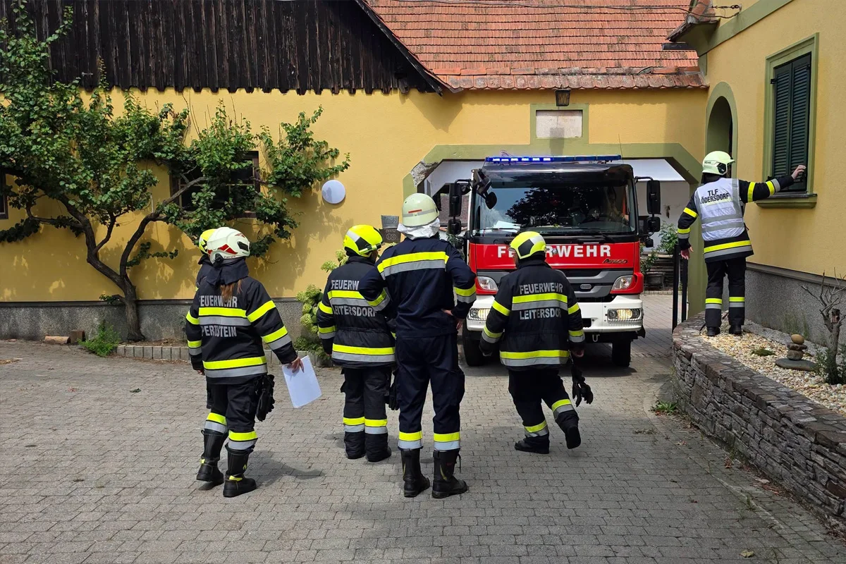 Eine Gruppe von Feuerwehrleuten in Einsatzkleidung steht vor einem roten Feuerwehrfahrzeug vor einem Gebäude.