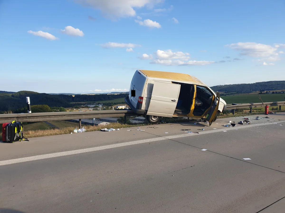 Ein weißer Lieferwagen steht schräg auf einer Leitplanke auf einer ländlichen Autobahn. Trümmer sind auf der Straße verteilt.