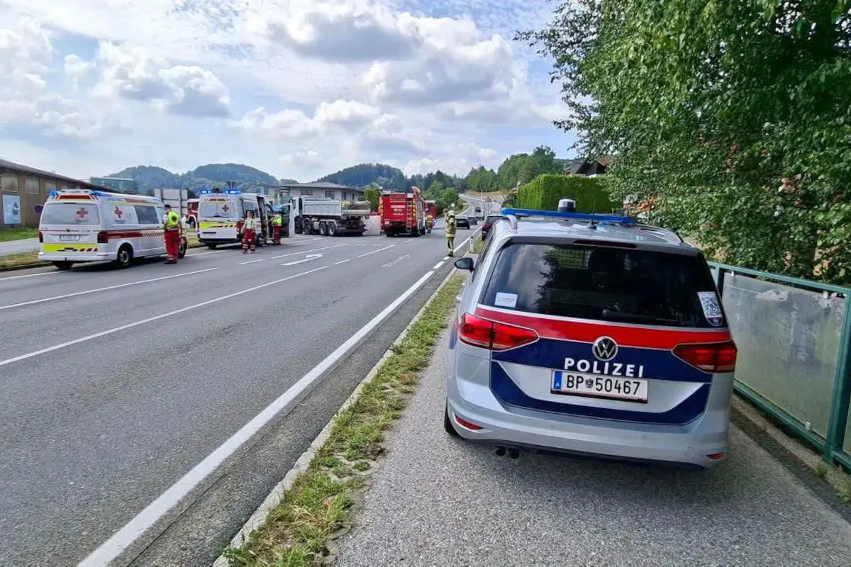 Ein Polizeiwagen steht auf einer Landstraße, während sich mehrere Rettungsfahrzeuge im Hintergrund befinden. Einsatzkräfte sind bei einem Lkw aktiv.