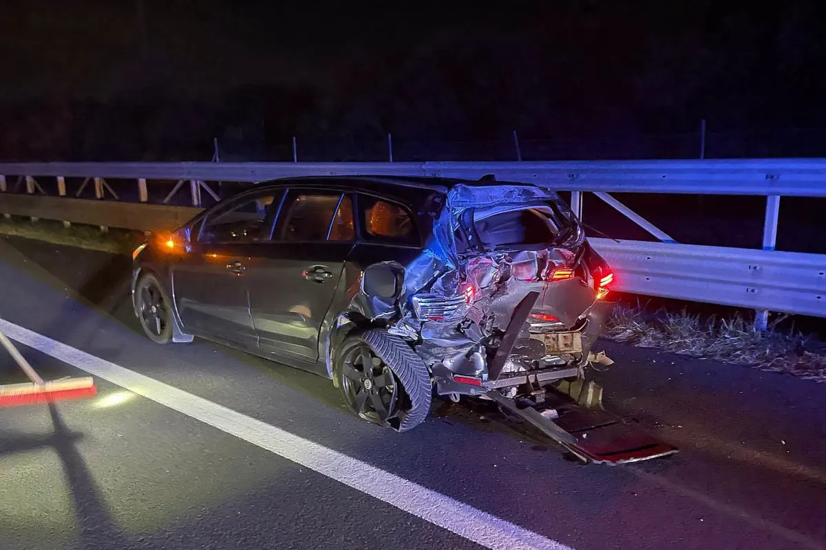 Ein Pkw mit erheblichem Heckschaden steht auf einer Autobahn bei Nacht neben einer Leitplanke.