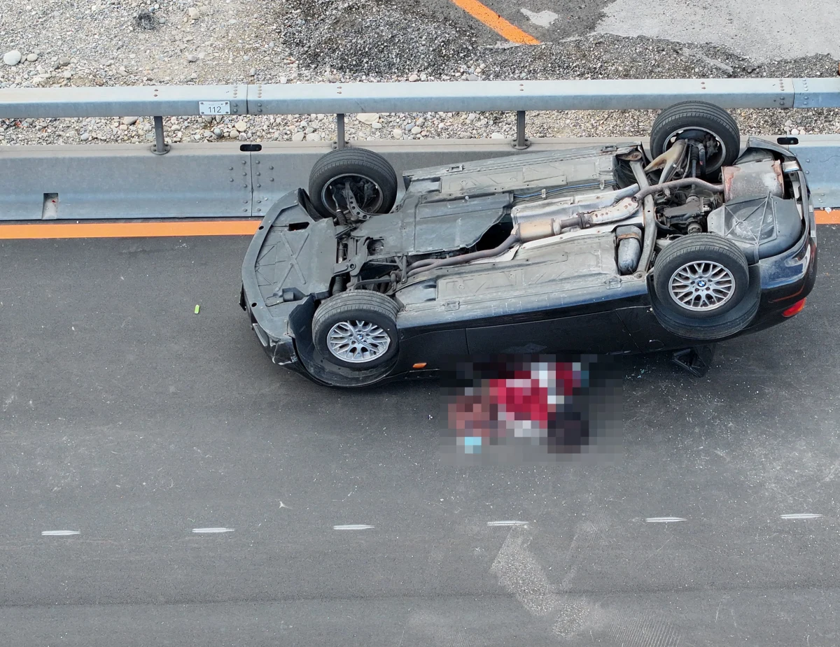 Ein Auto liegt auf dem Dach auf einer Autobahn, neben dem Fahrzeug ist etwas verpixelt dargestellt.