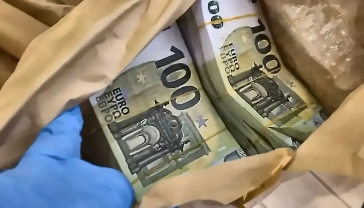 Ein Bündel mit 100-Euro-Scheinen, das in braunem Papier verpackt ist, wird mit einer behandschuhten Hand gehalten.