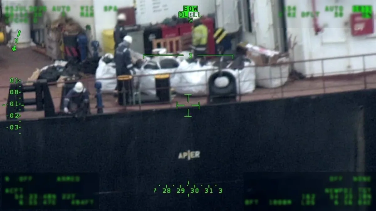 Das Bild zeigt mehrere Personen auf einem Schiff, die in der Nähe großer weißer Säcke stehen. Es handelt sich um eine Überwachungskamera-Aufnahme mit digitalen Anzeigen im Bild.