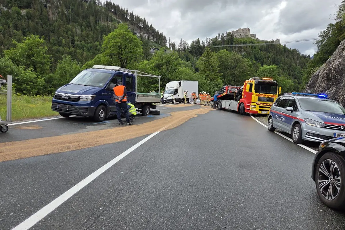 Eine Landstraße mit Einsatzfahrzeugen, darunter ein Polizeiauto, Abschleppwagen und ein Lieferwagen. Personen tragen orange Warnwesten.