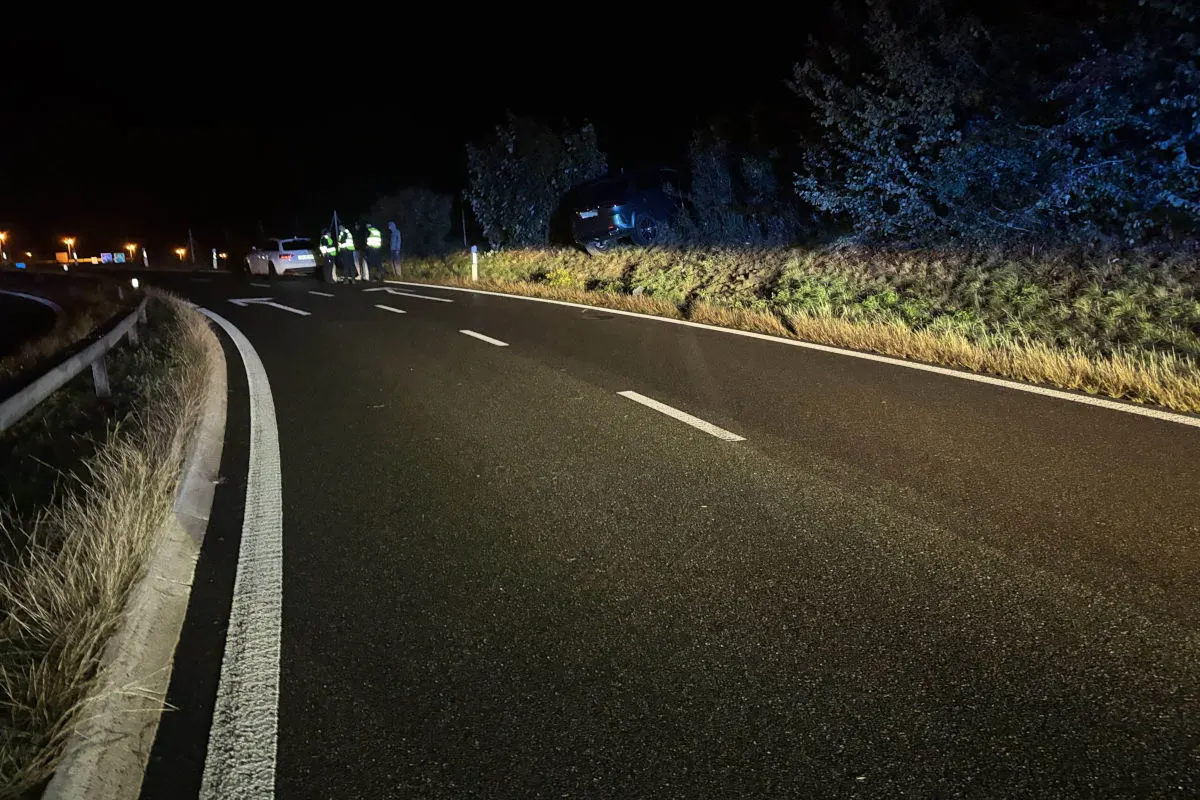 Bei Nacht ist ein Auto von der Straße abgekommen und im Graben gelandet, während sich Einsatzkräfte auf der Straße befinden.