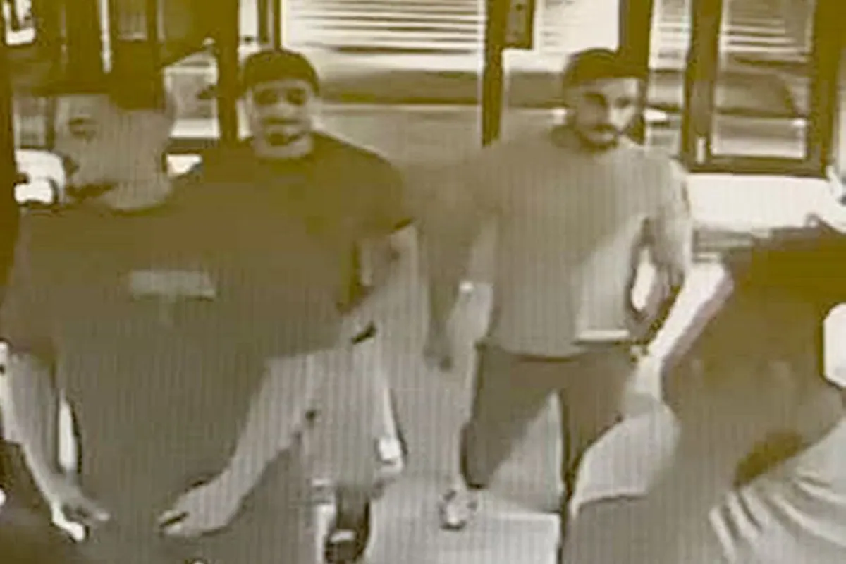 Ein körniges Überwachungskamerabild zeigt vier Personen beim Betreten eines Gebäudes durch einen Eingangsbereich.