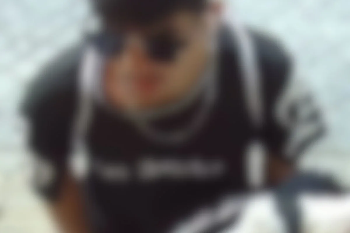 Eine unscharfe Aufnahme zeigt eine Person in dunkler Kleidung und mit Sonnenbrille. Die Umgebung ist verschwommen.