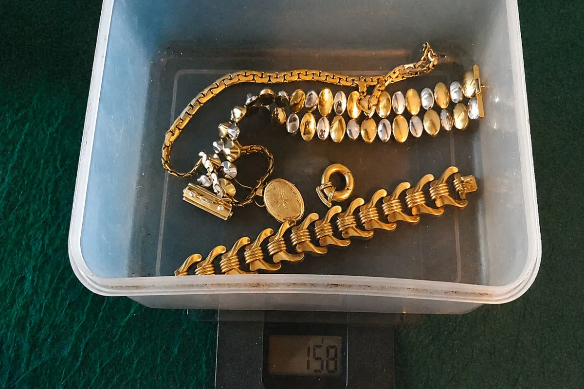 Mehrere goldene Schmuckstücke liegen in einer durchsichtigen Plastikbox, die auf einer Waage mit 158 g angezeigt wird.