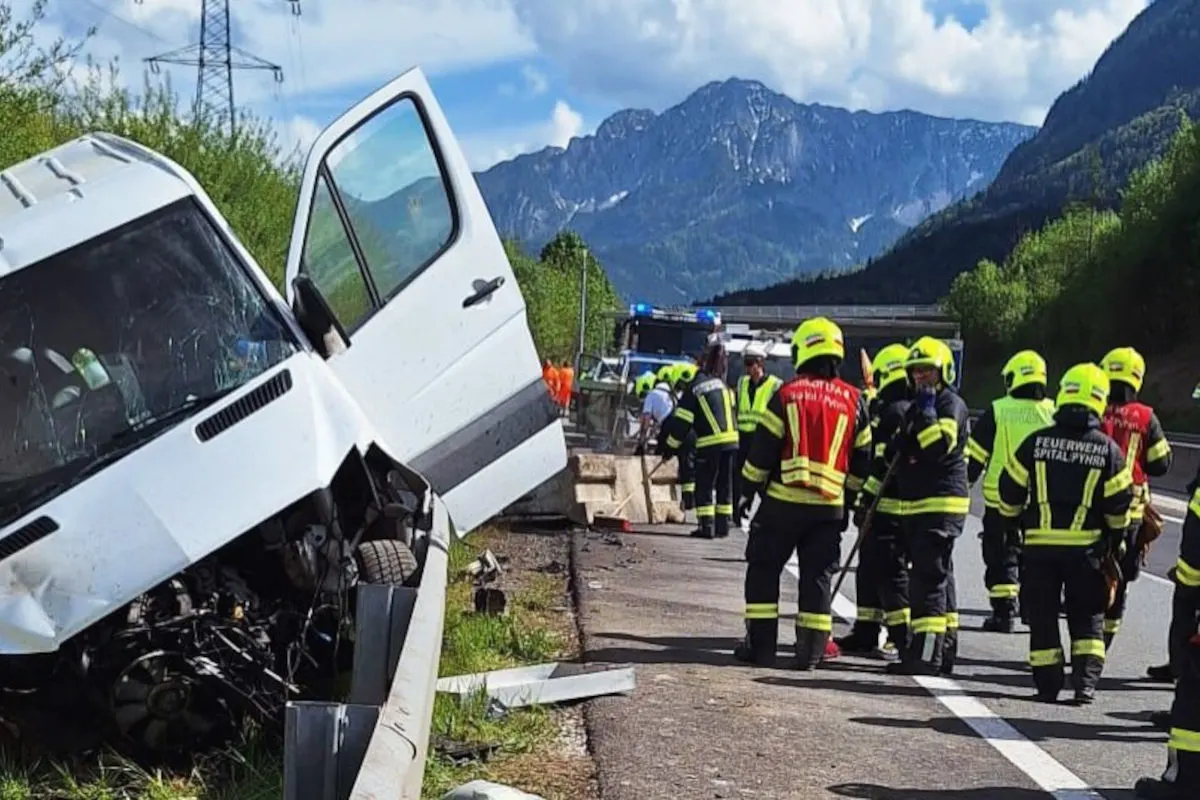 Ein weißer Lieferwagen steht beschädigt an einer Leitplanke auf einer Autobahn. Mehrere Feuerwehrleute sind an der Unfallstelle aktiv.