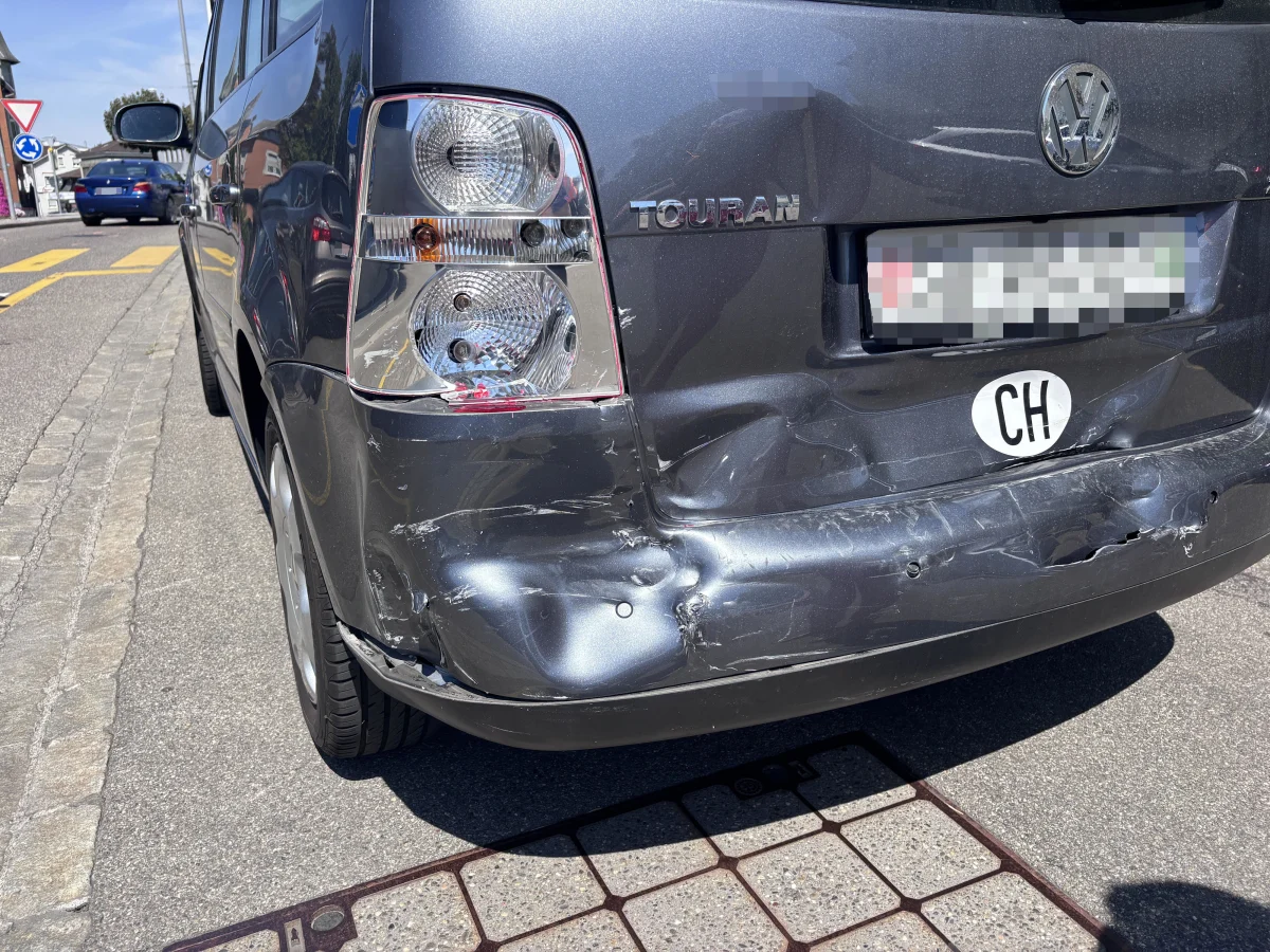 Das Heck eines grauen VW Touran zeigt deutliche Dellen und Kratzer an der Stoßstange, erkennbar auf einer Straße.