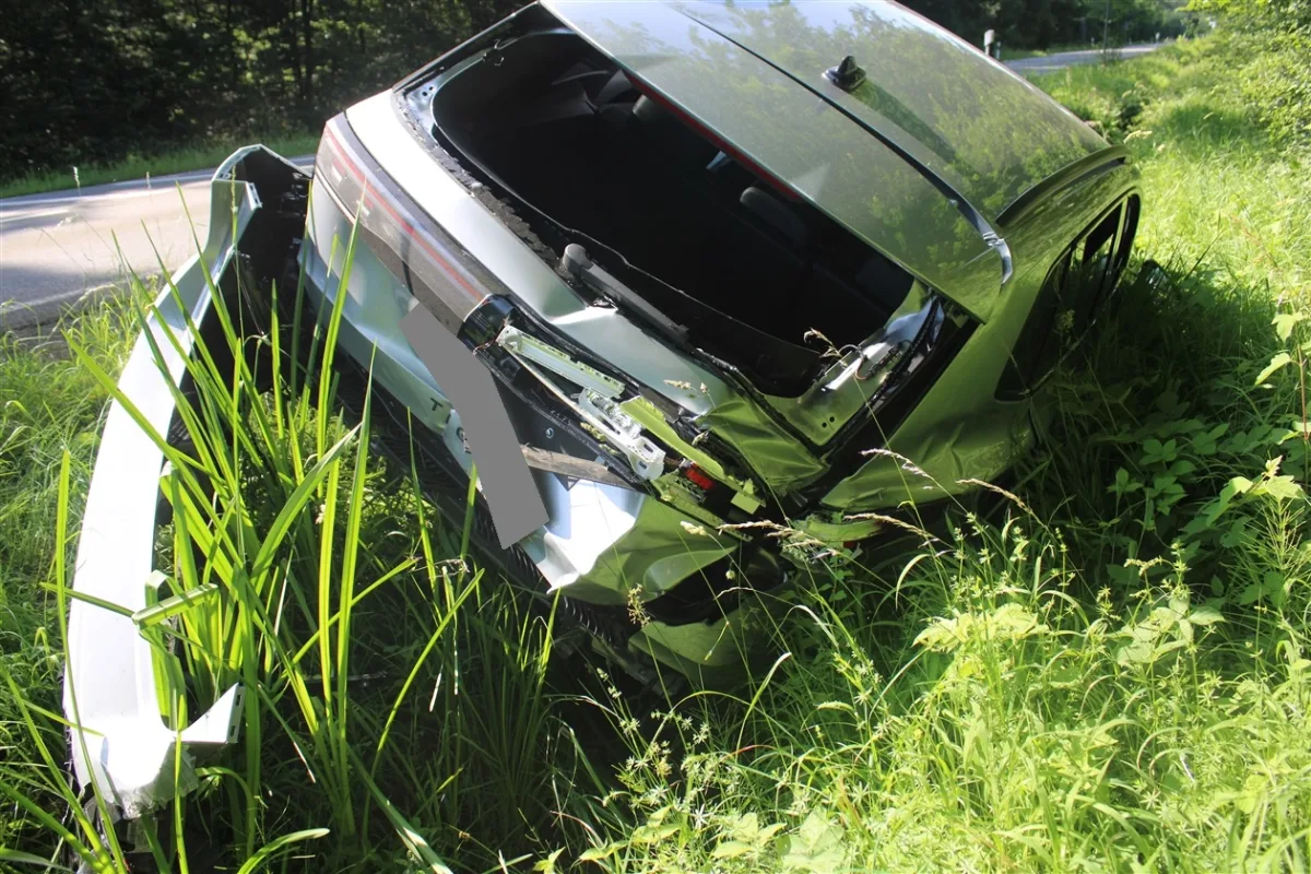 Ein graues Auto liegt mit stark beschädigtem Heck im grünen Straßengraben neben einer Landstraße.