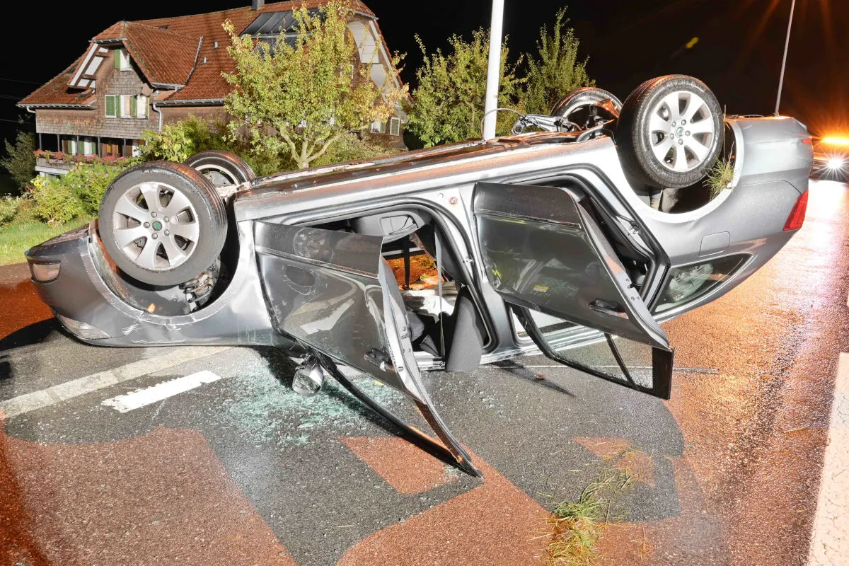 Ein silbernes Auto liegt auf dem Dach auf der Straße, die Türen sind geöffnet, und es ist Nacht.
