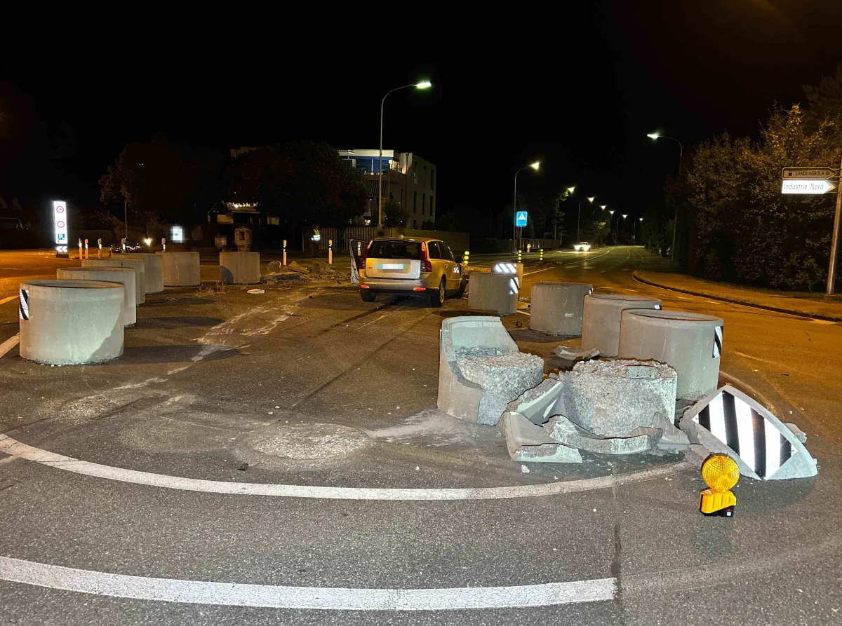 Ein Auto steht bei Nacht auf einer Straße neben beschädigten Betonbarrieren. Die Straße ist unbeleuchtet und leer.