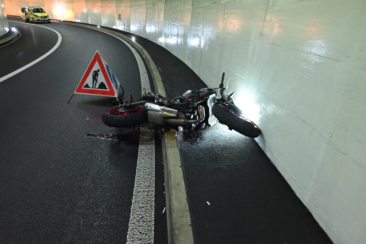 Ein umgekipptes Motorrad liegt auf der Straßenseite in einem beleuchteten Tunnel. Daneben steht ein Warndreieck.
