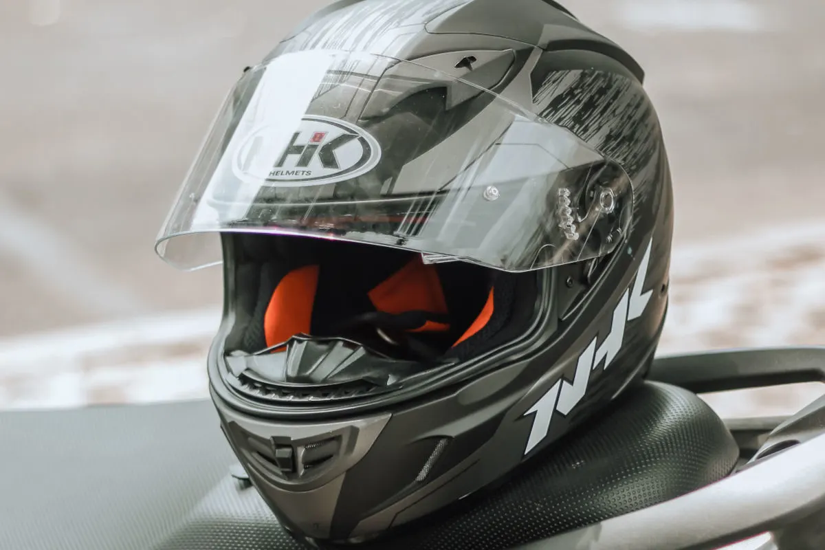 Ein schwarzer Integralhelm mit transparentem Visier liegt auf einem Motorrad. Der Helm hat ein markantes H-K-Helmets-Logo.