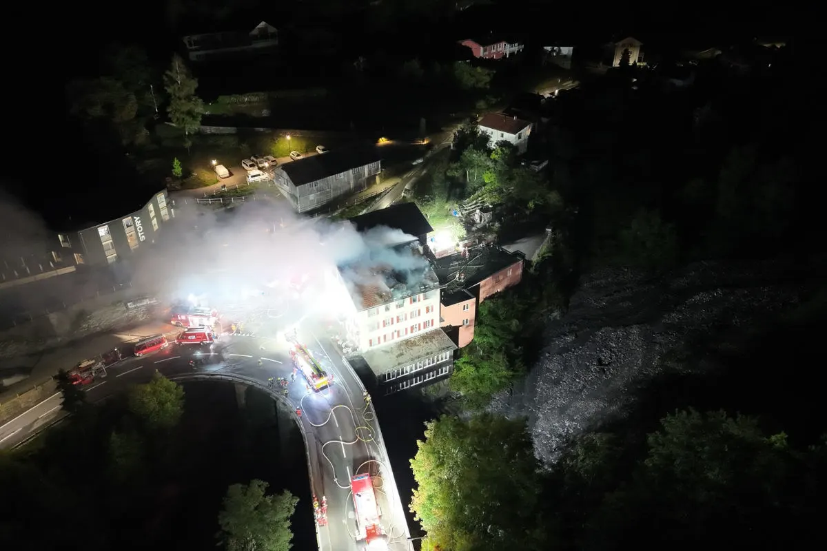 Das Bild zeigt einen nächtlichen Brand in einem mehrstöckigen Gebäude. Mehrere Feuerwehrfahrzeuge sind vor Ort, Rauch steigt auf.
