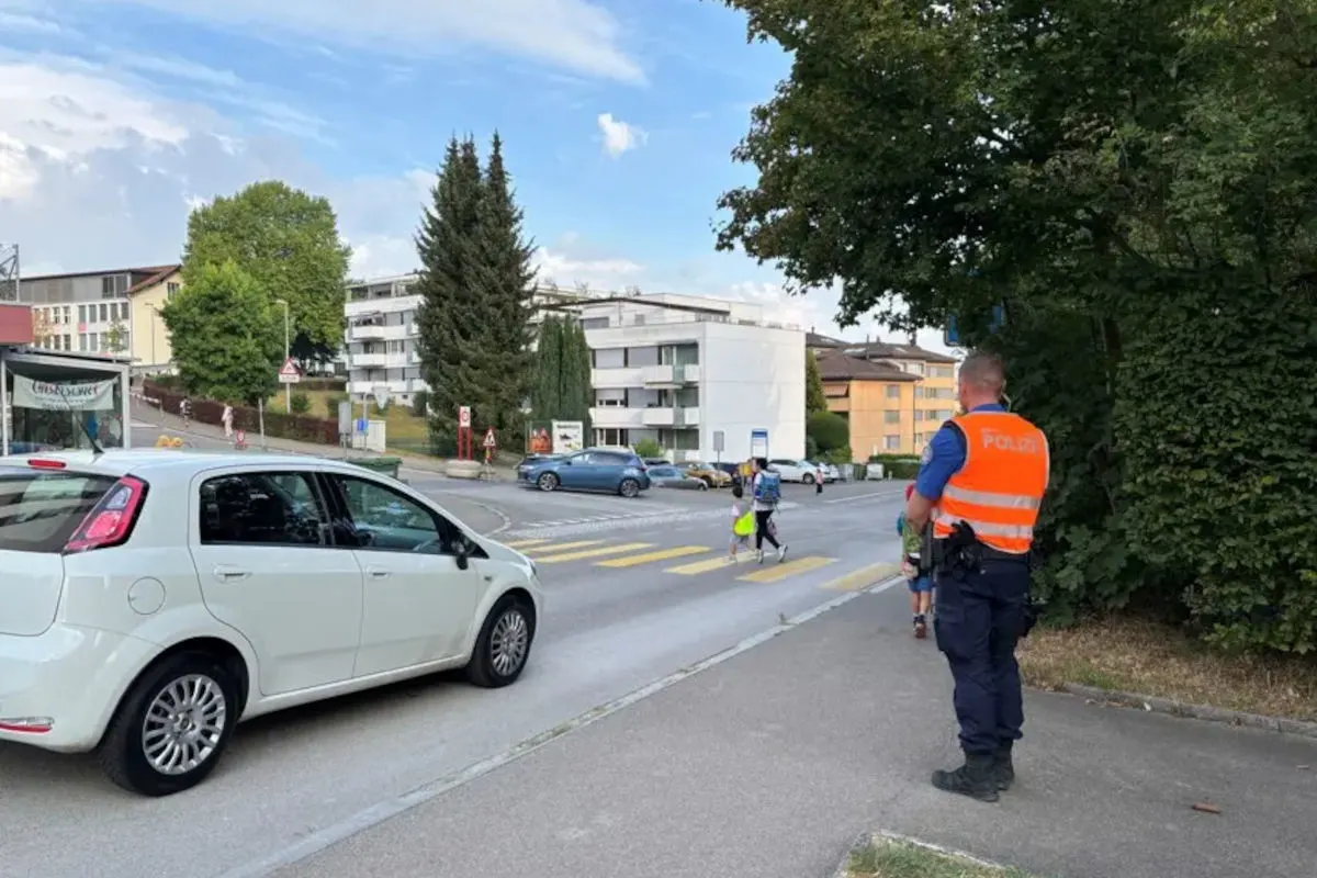 Ein Polizist steht an einem Zebrastreifen in einer Stadt, beobachtet den Verkehr und sorgt für die Sicherheit von Fußgängern, darunter Schulkinder.