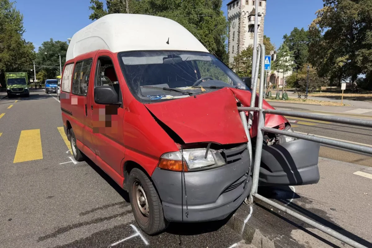 Ein roter Van mit beschädigter Front ist in ein Metallgeländer gefahren. Im Hintergrund sind Bäume und ein historisches Gebäude sichtbar.