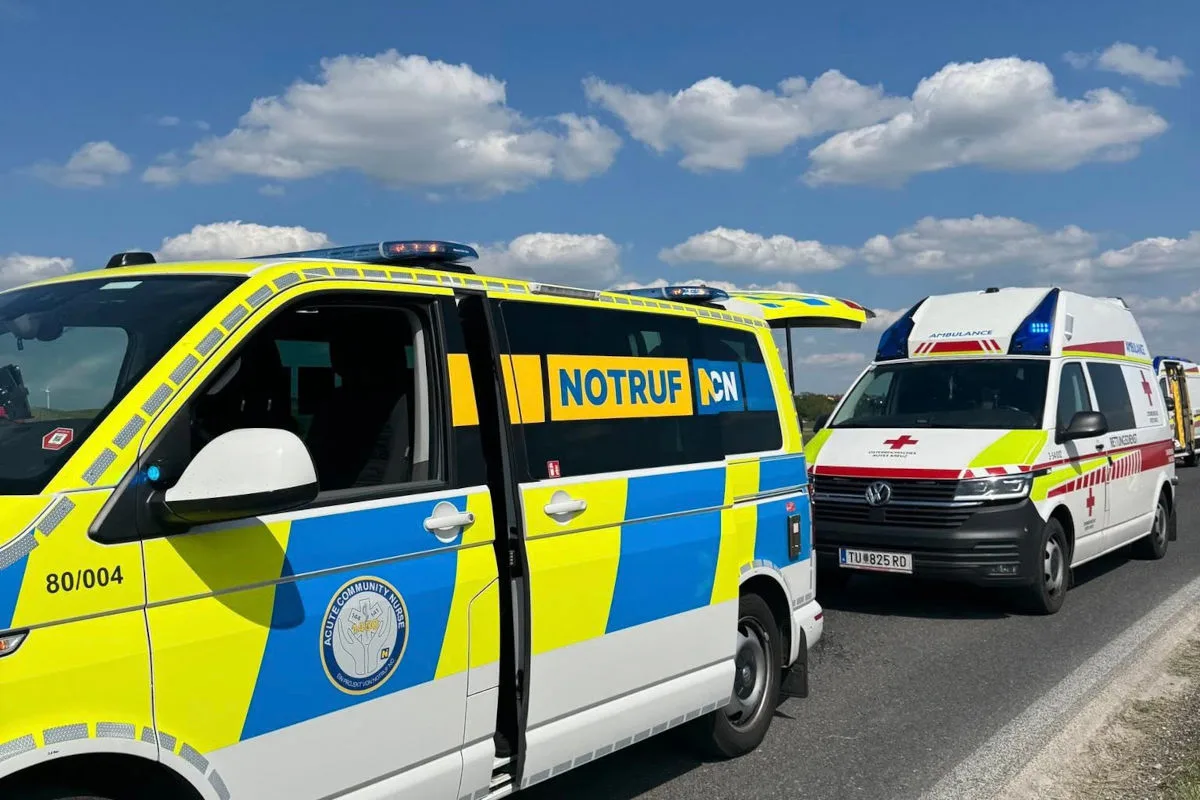 Ein gelbes Notruf-Fahrzeug und ein weiß-rotes Ambulanzfahrzeug stehen nebeneinander auf einer Landstraße. Der Himmel ist klar und sonnig.