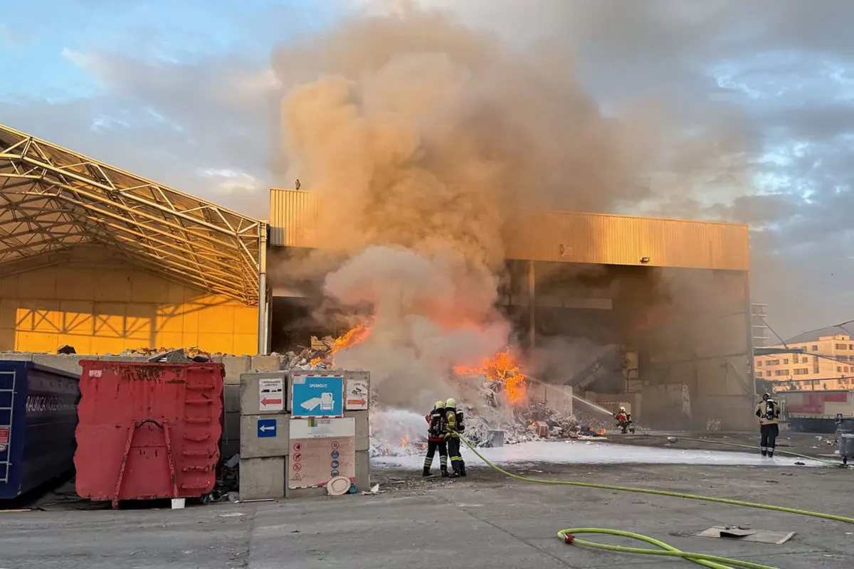 Zwei Feuerwehrleute bekämpfen einen großen Brand in einem Industriegebäude. Dichte Rauchschwaden steigen auf.